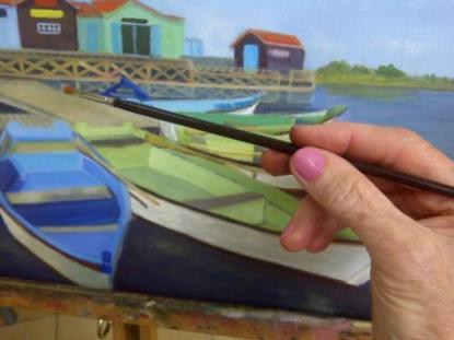une main tient un pinceau et peint des barques de pêche